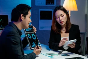 Two business colleagues analyzing AI vs reactive maintenance performance data on tablet and smartphone in modern office